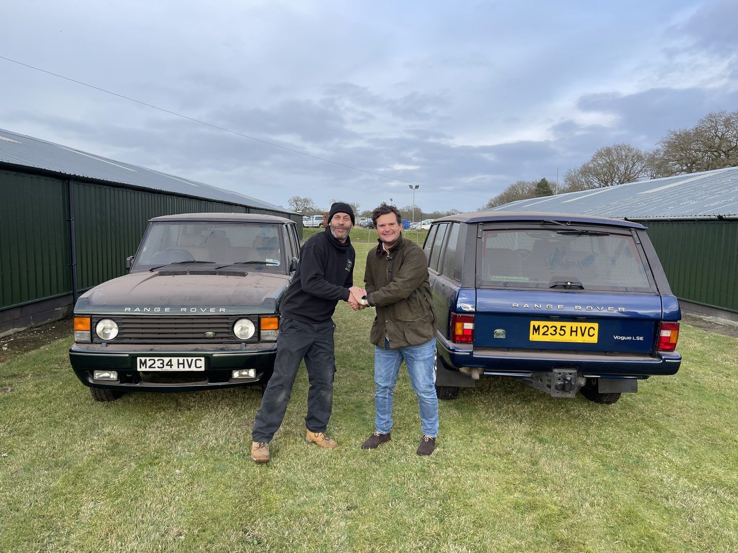 Two people shaking hands between two Range Rovers on grass