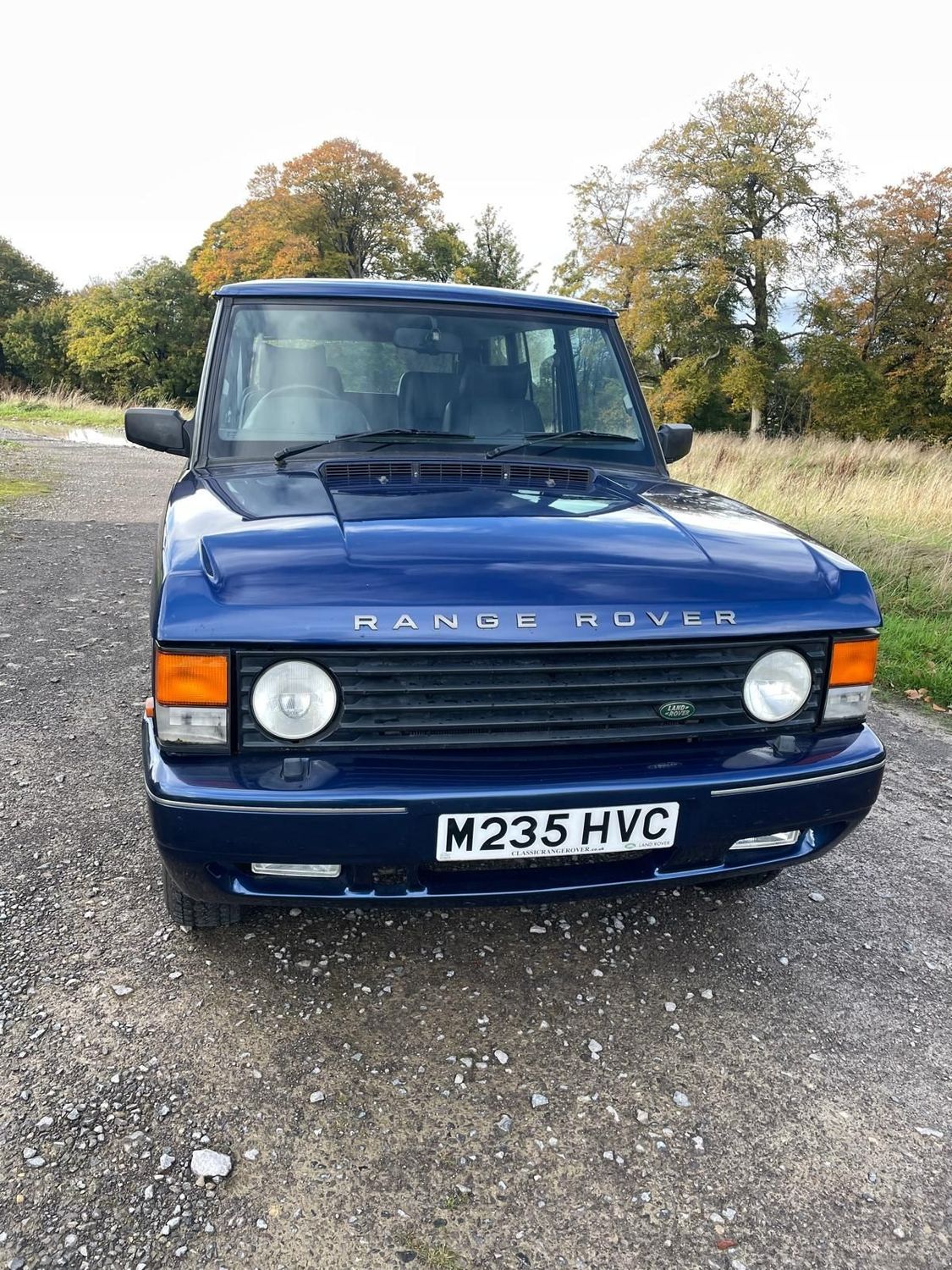 A navy Range Rover Classic on a driveway, autumn trees behind