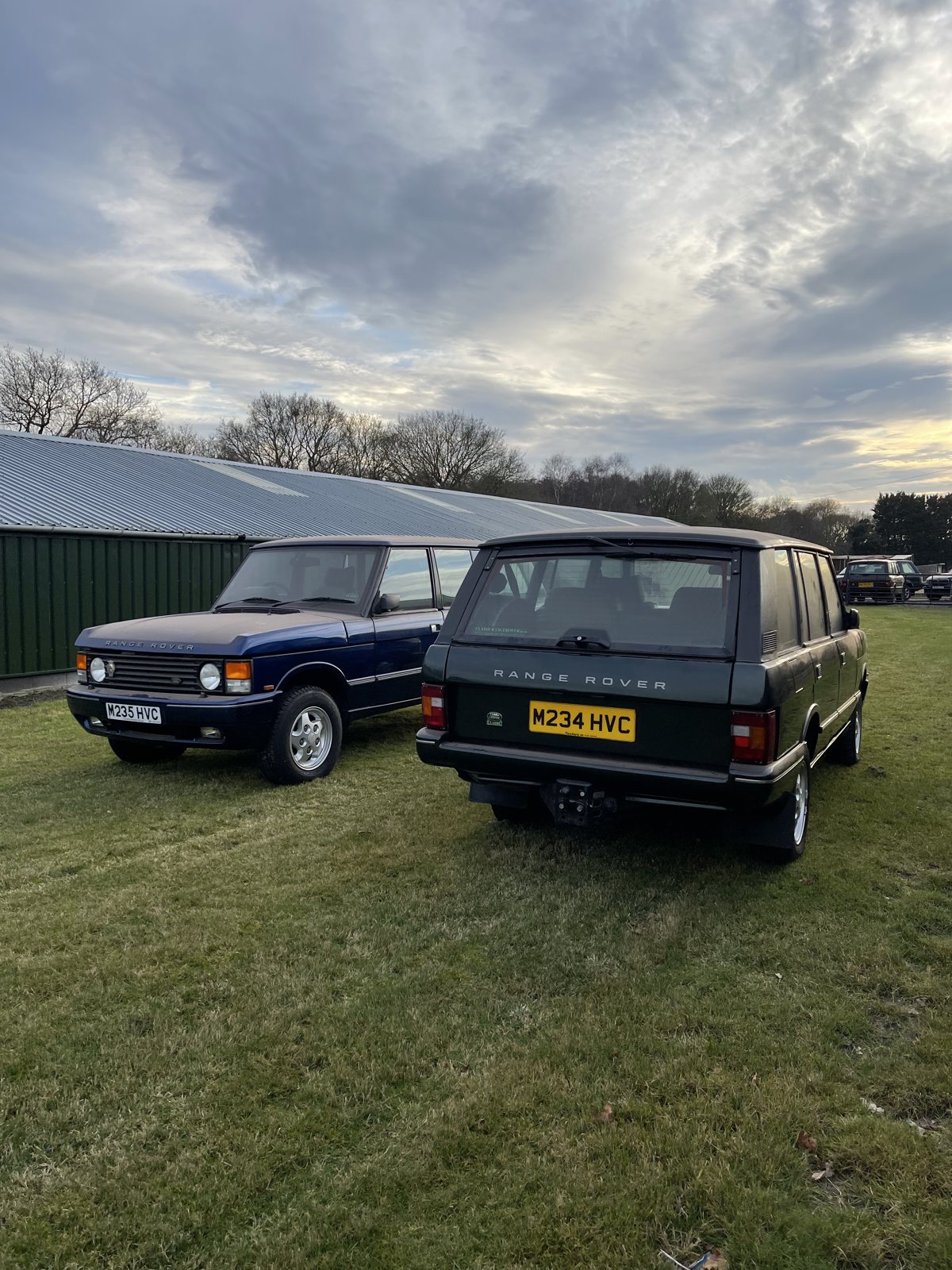 A matched pair of classic Range Rovers at dusk in a field